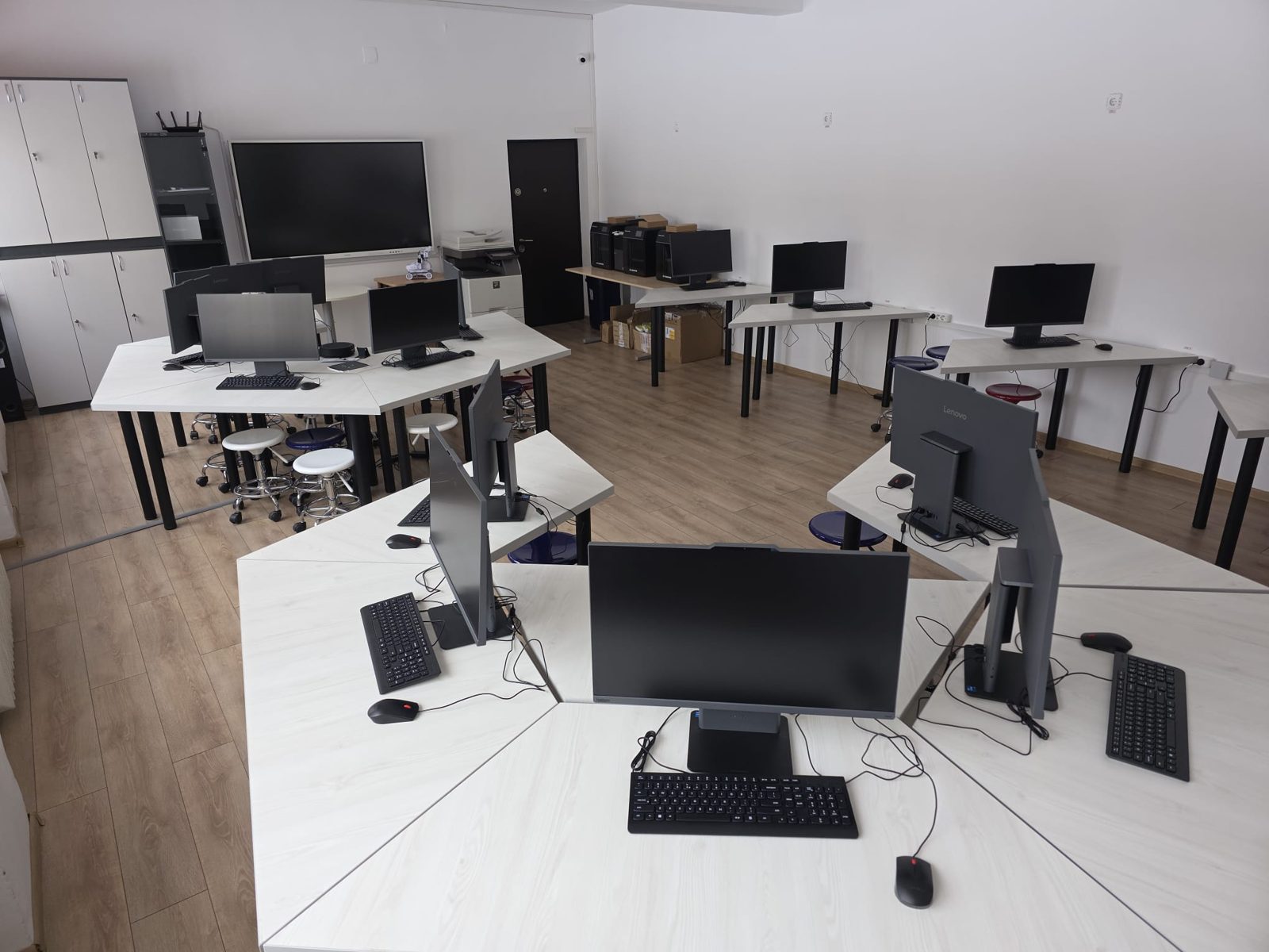 Laborator SmartLab: mese albe așezate în grupuri de lucru, stații de lucru cu monitoare și tastaturi, ecran interactiv mare pe perete